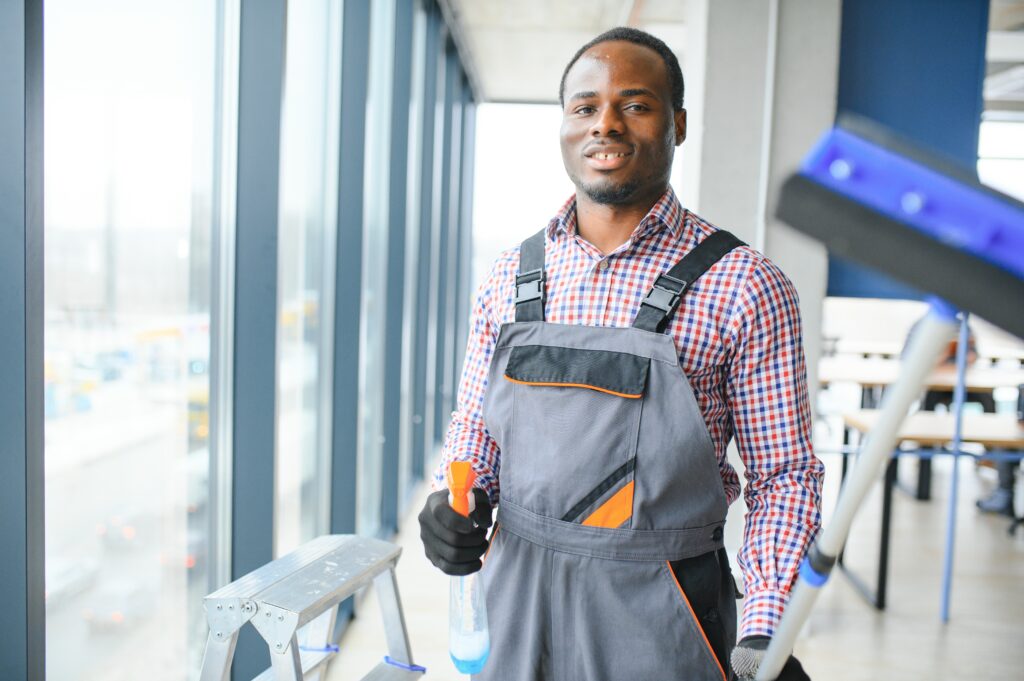 Happy Male Worker Cleaning Glass With Squeegee And Spray Bottle