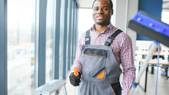 Happy Male Worker Cleaning Glass With Squeegee And Spray Bottle