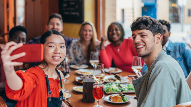 Asian woman taking a selfie at a multiethnic gathering of friends in a restaurant